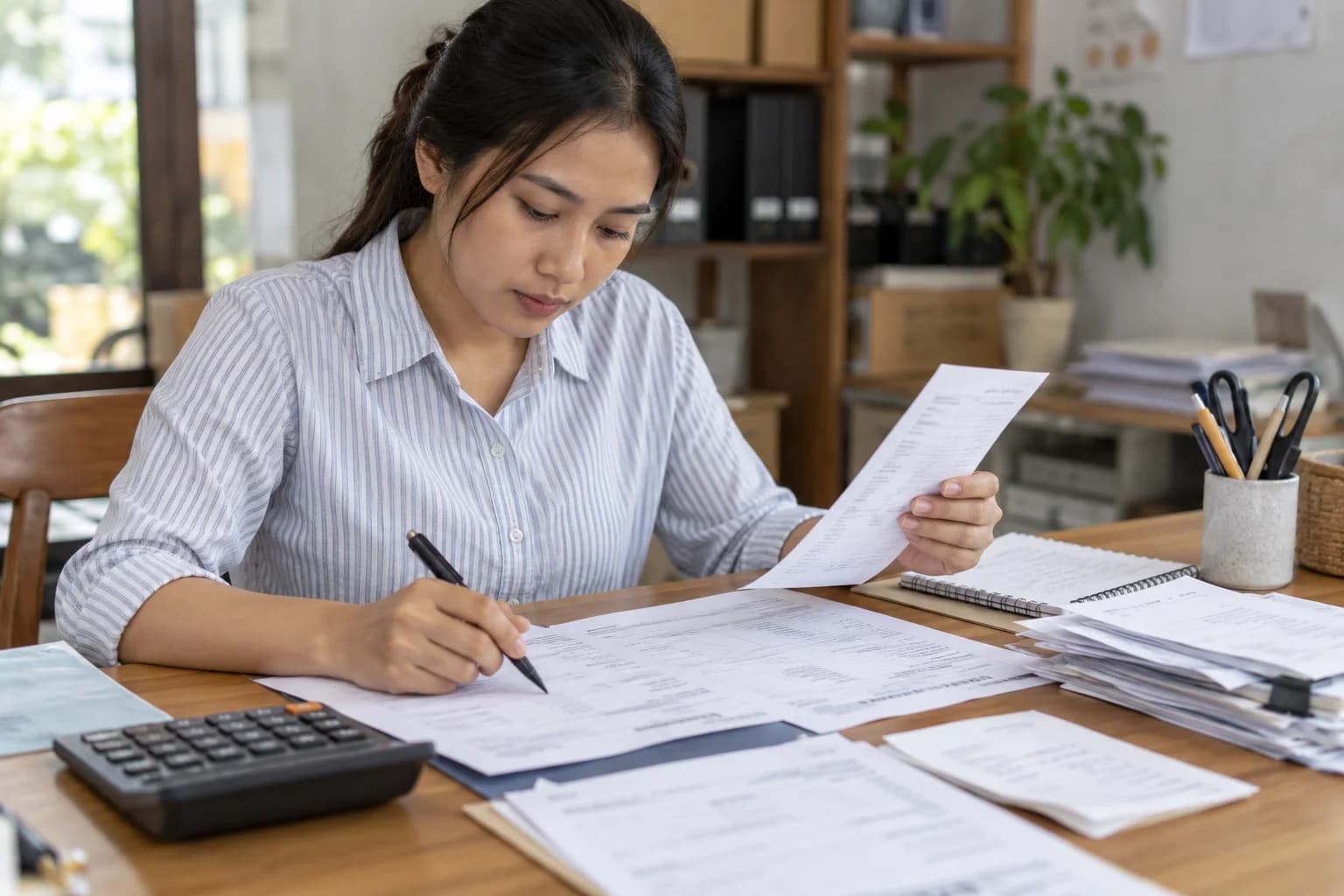 Admin keuangan memeriksa lembar invoice dan tanda terima di atas meja kerja.